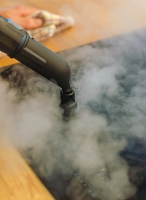 Close-up of a steam cleaner nozzle releasing steam onto induction stove